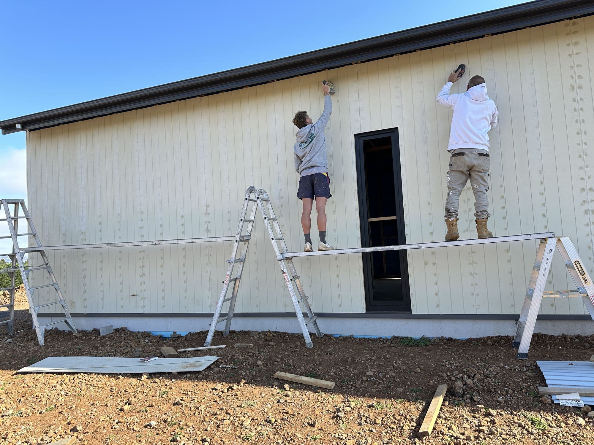 Two Tricoat painters on ladders repainting a white weatherboard exterior