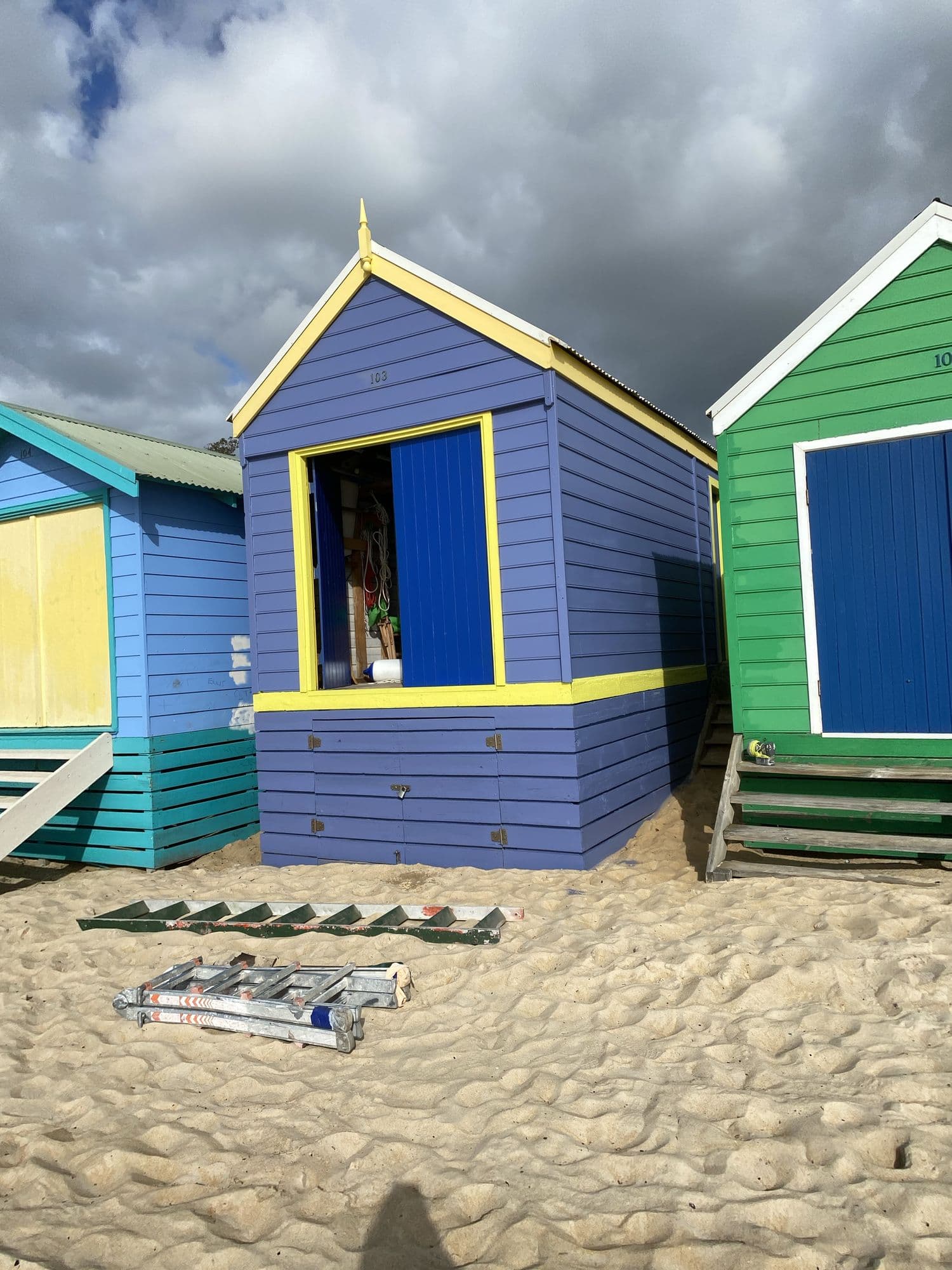 Brightly repainted blue, yellow and green bathing boxes on a Melbourne bayside beach