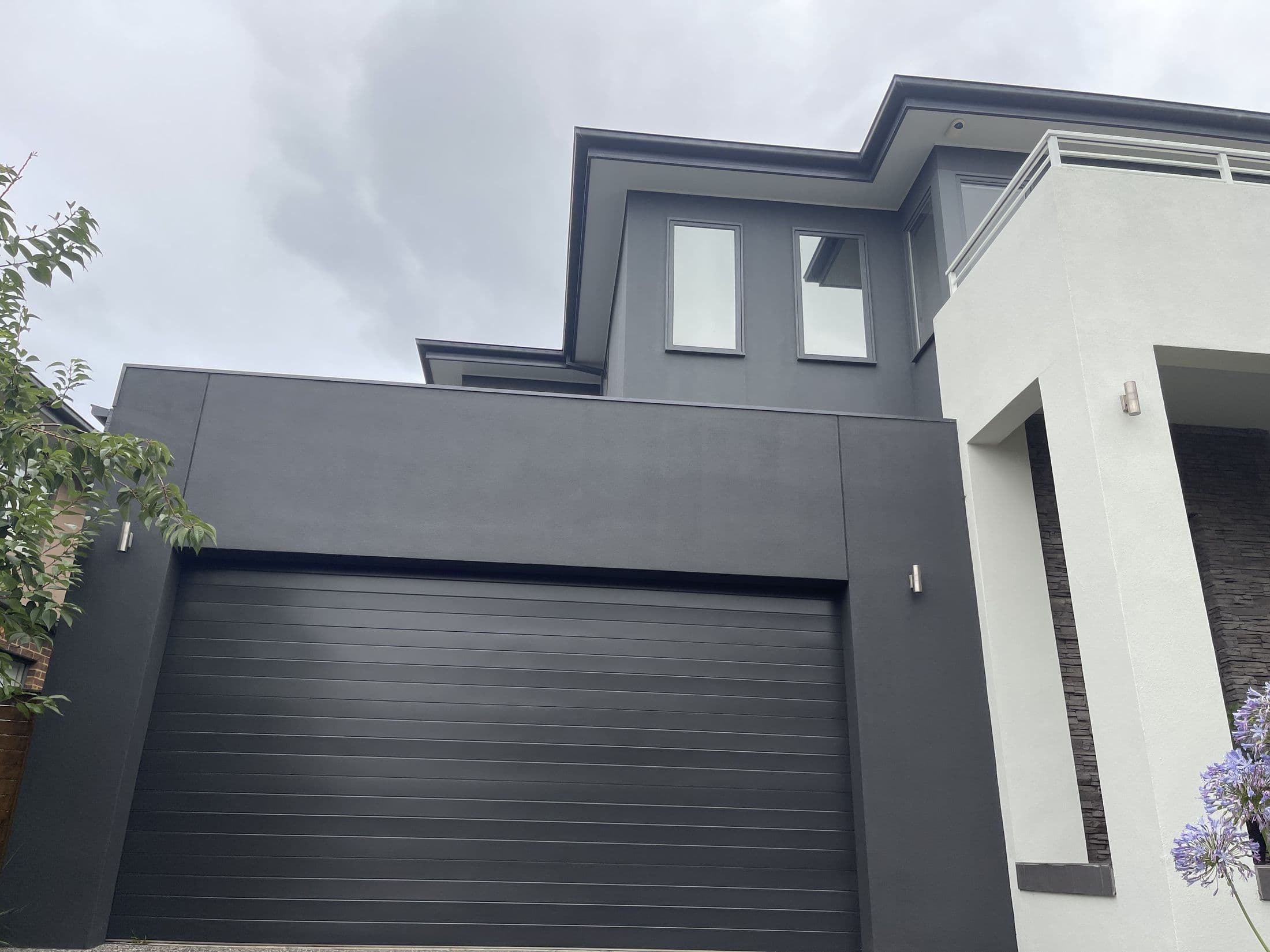 Newly painted charcoal two-storey home exterior against a dramatic sky