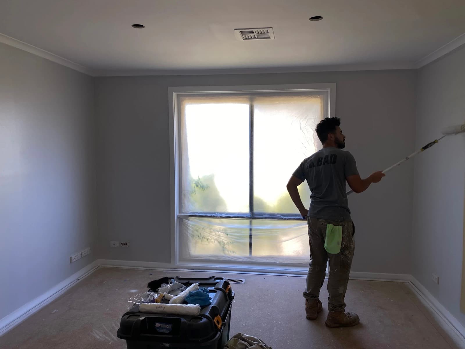 Tricoat painter rolling the first coat in a fully masked and sheeted room — preparation stage