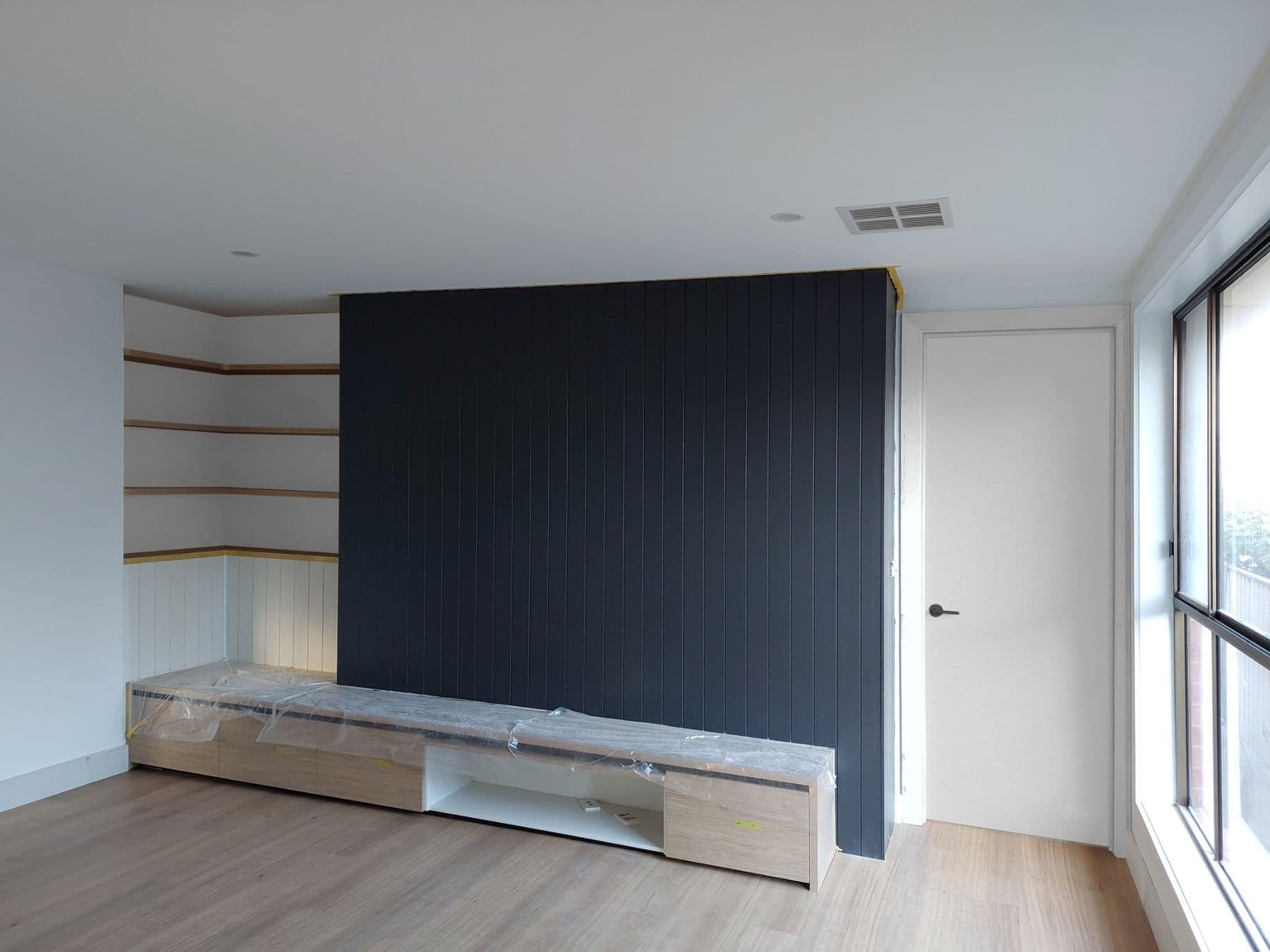 Charcoal vertical-batten feature wall behind a floating timber media unit in a finished living room